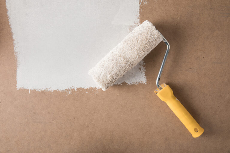 Paint roll brush in white paint on plywood surface